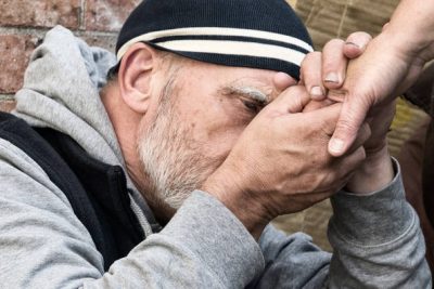 homeless man holding the hand of another person